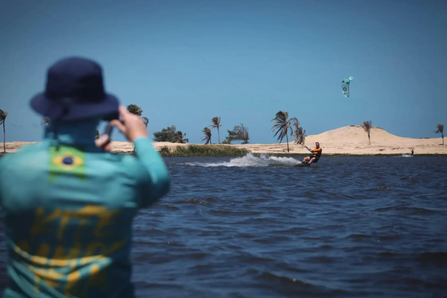 Kitesurfer płynący na spokojnej wodzie, brazylijska plaża w tle, wiatraki palmy poruszane wiatrem